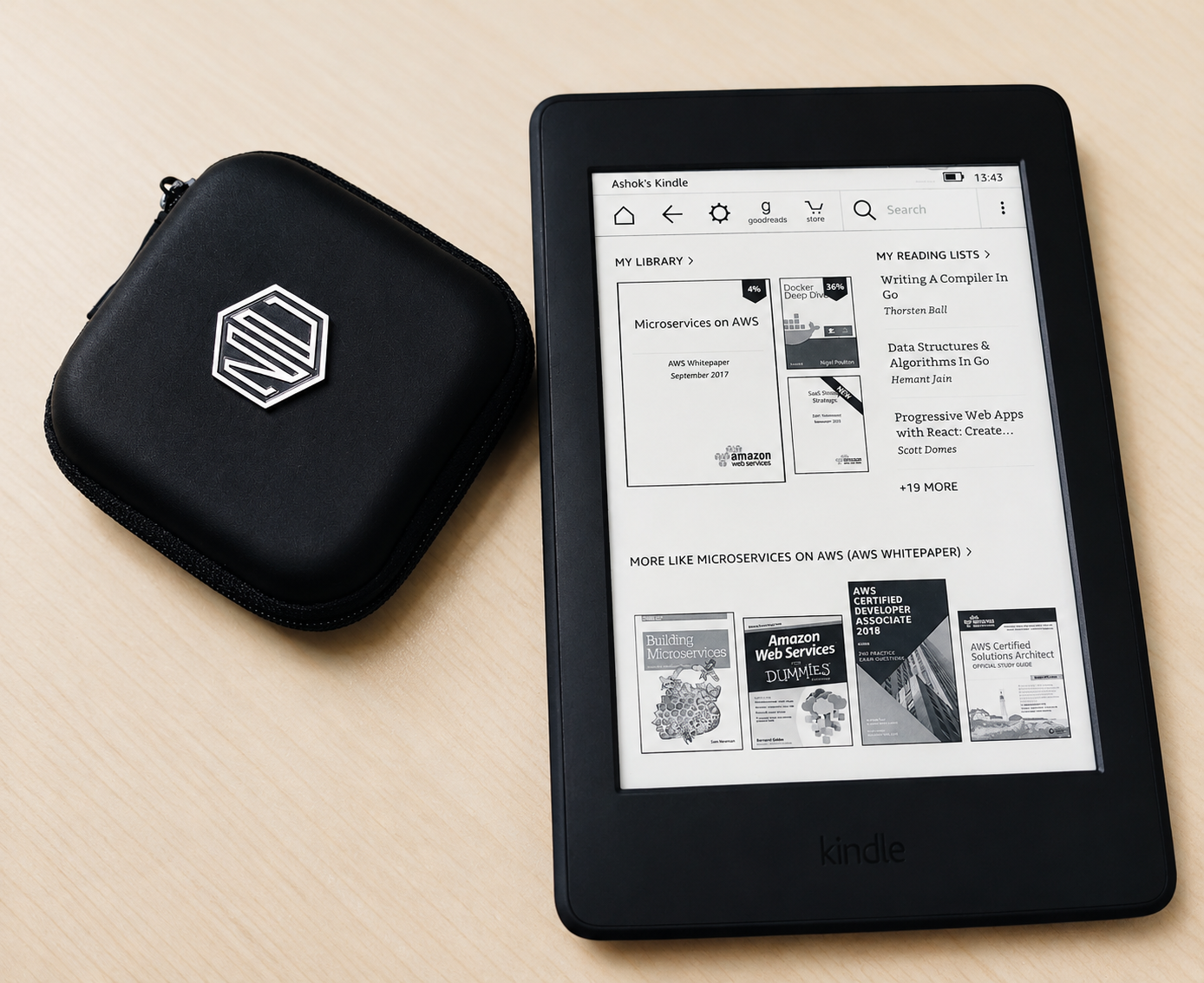 A Kindle showing a library of AWS, Docker and Go titles, beside a zipped accessory case